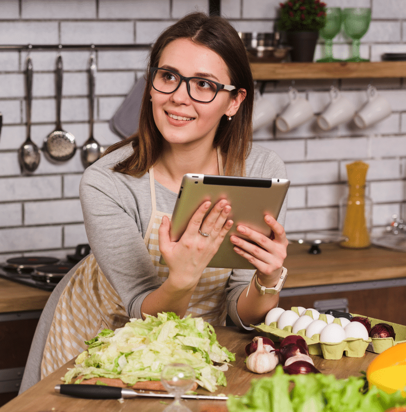 About me 1 Woman in apron holding a tablet while preparing fresh vegetables in a modern kitchen